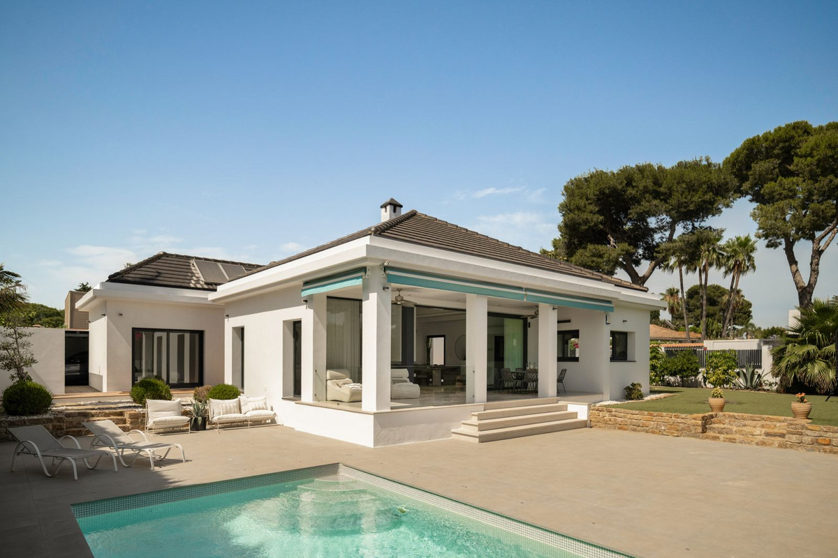 Single-storey white villa with full-height glass opening onto the pool and covered terrace