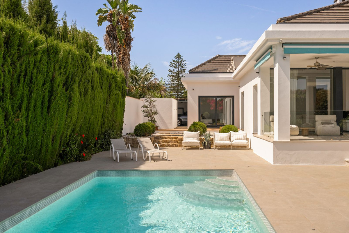 Pool with sun loungers, cypress hedge and terrace facing the villa’s open glass front