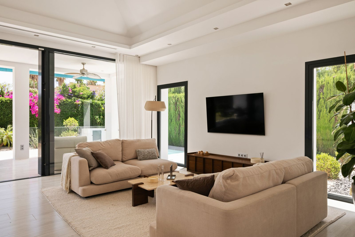 Beige upholstered sofas facing a television wall with views to the terrace and pool