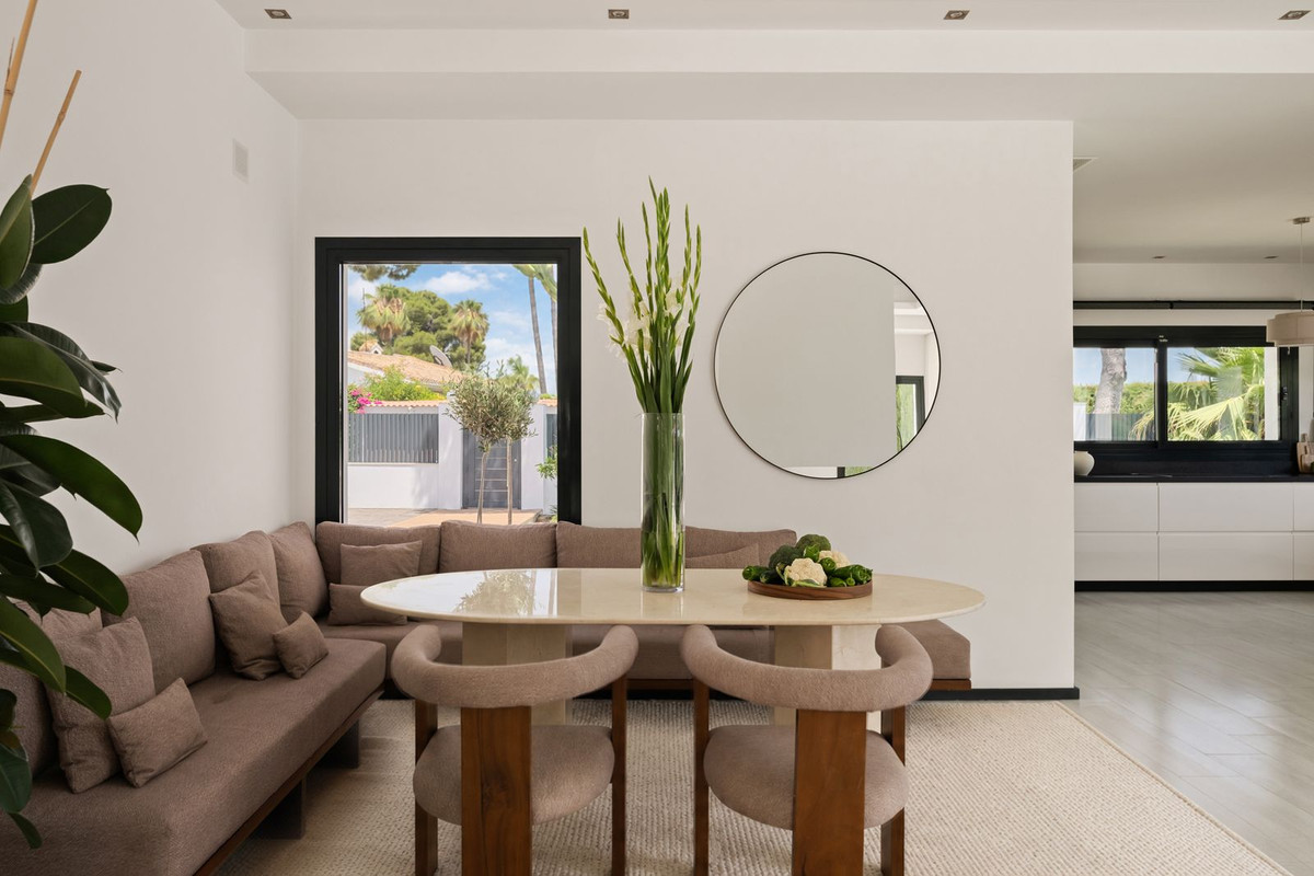 Dining area with oval travertine table, upholstered banquette and round mirror