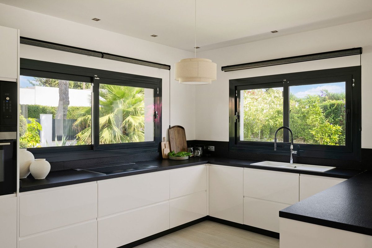 L-shaped kitchen with white cabinet fronts, black worktop and two windows to the garden