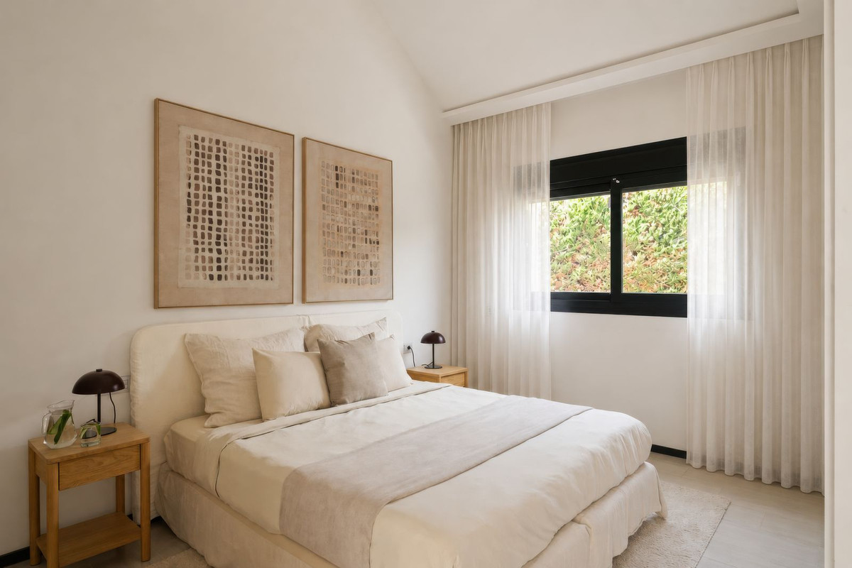 Light bedroom with upholstered headboard, artwork and window onto greenery